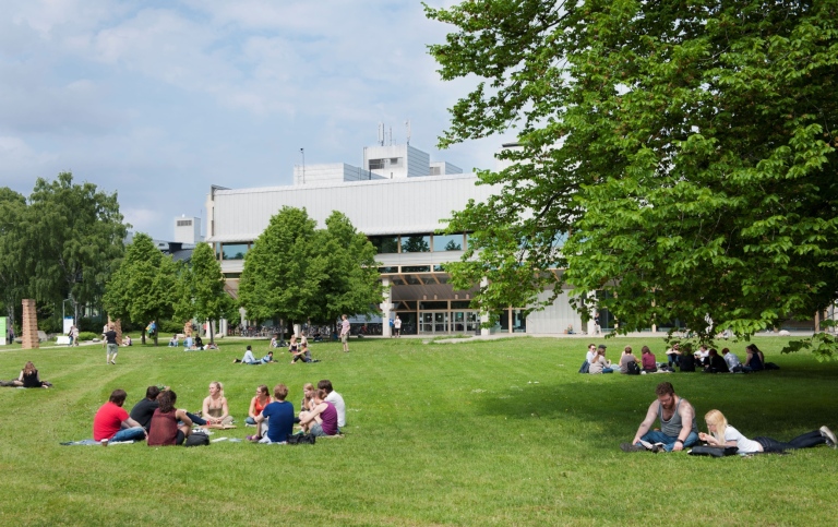 Studenter sitter på gräsmattan mitt på campus framför Arrheniuslaboratoriet. Foto: Eva Dalin.